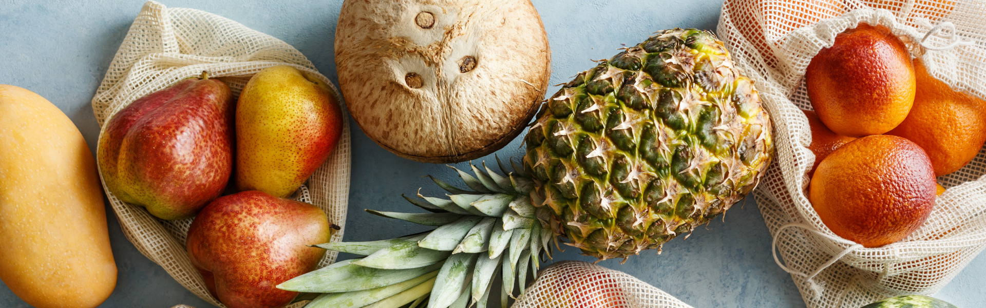 Verschiedene frische Obstsorten in wiederverwendbaren Netztaschen, darunter Äpfel, Birnen, Pfirsiche, Ananas, Melonen und Orangen. Verschiedene frische Obstsorten in wiederverwendbaren Netztaschen, darunter Äpfel, Birnen, Pfirsiche, Ananas, Melonen und Orangen.