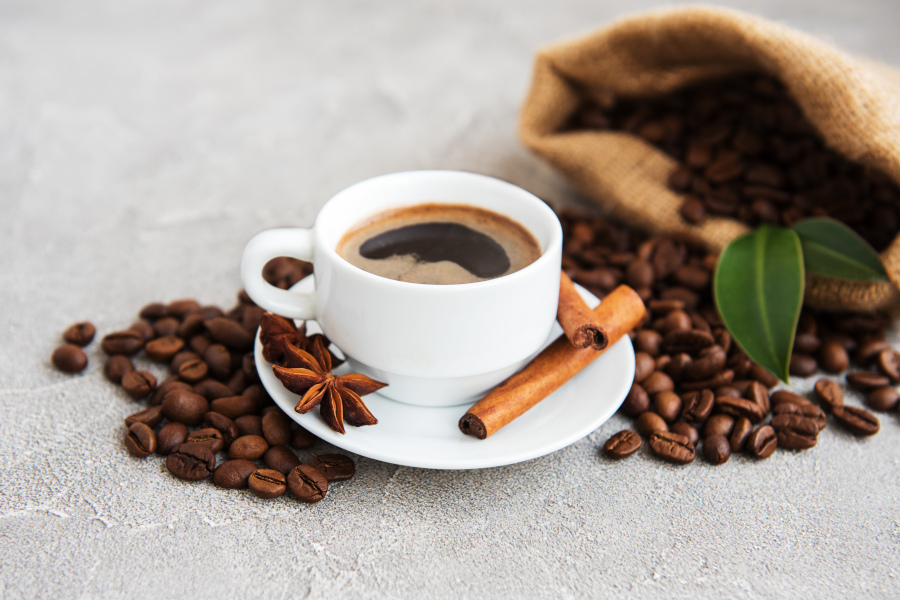 Tasse frisch gebrühter Kaffee mit Zimtstange, Sternanis und Kaffeebohnen – daneben ein Jutesack mit Kaffeebohnen Tasse frisch gebrühter Kaffee mit Zimtstange, Sternanis und Kaffeebohnen – daneben ein Jutesack mit Kaffeebohnen